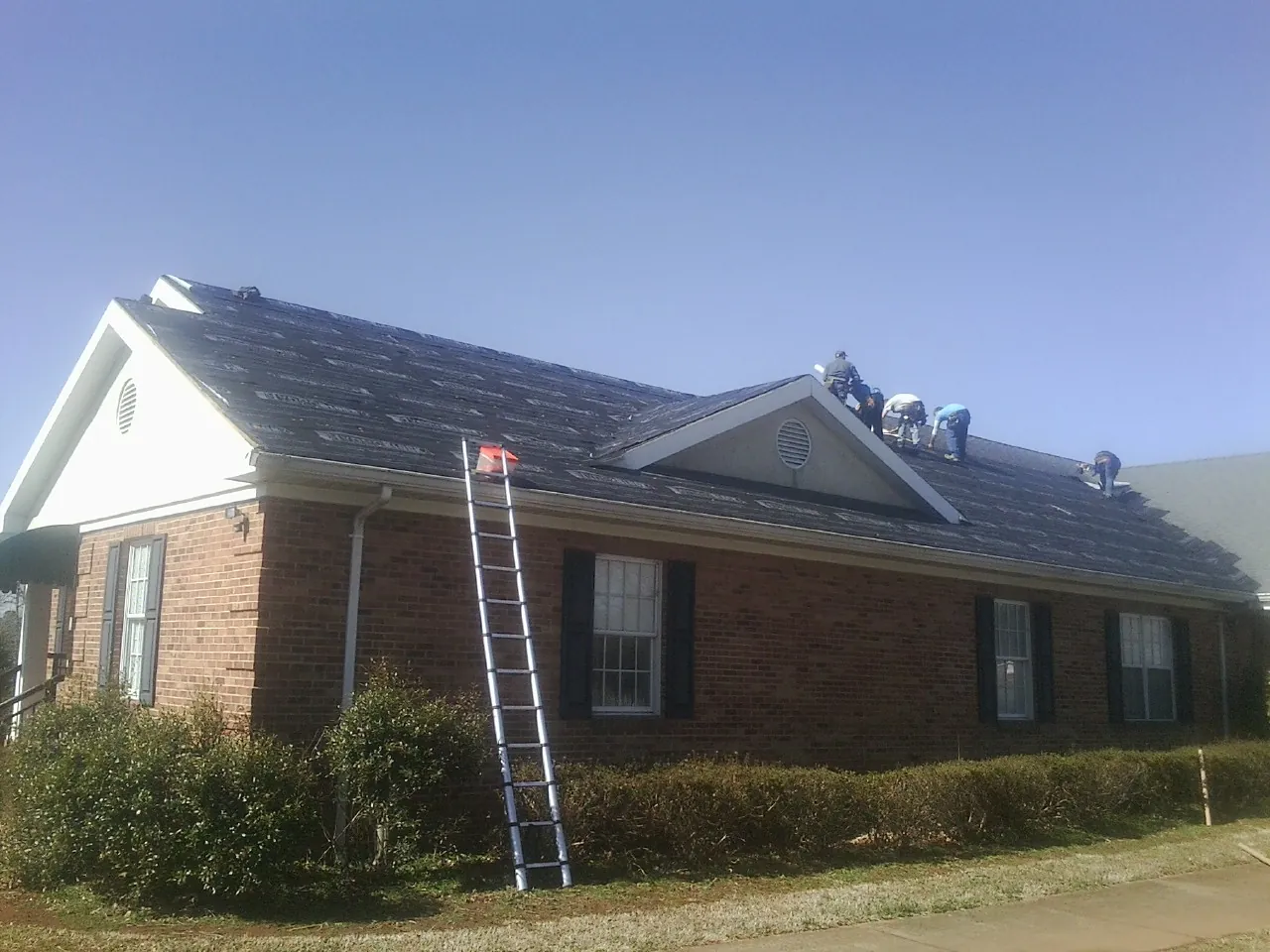 Crew tearing shingles off a brick ranch roof with a ladder set — Emergency Roof Repair work by our crew in Boaz