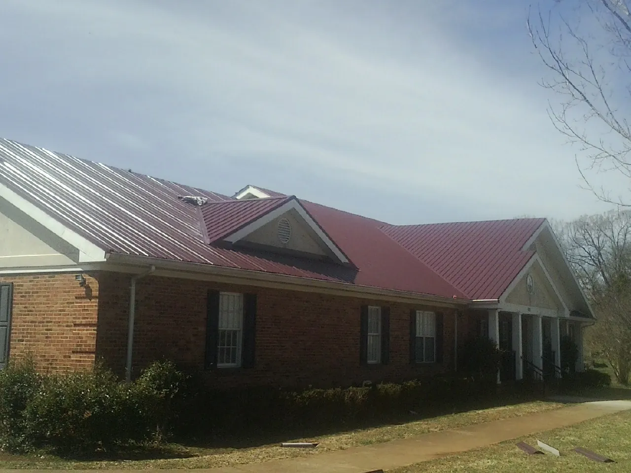 Red metal roof with gabled entries on a long brick building, from a Hail Damage Roof Repair job in Boaz