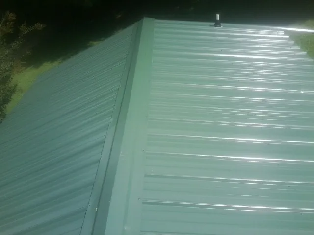 New green metal panels meeting at the ridge of a roof — Flat Roof Repair work by our crew in Boaz