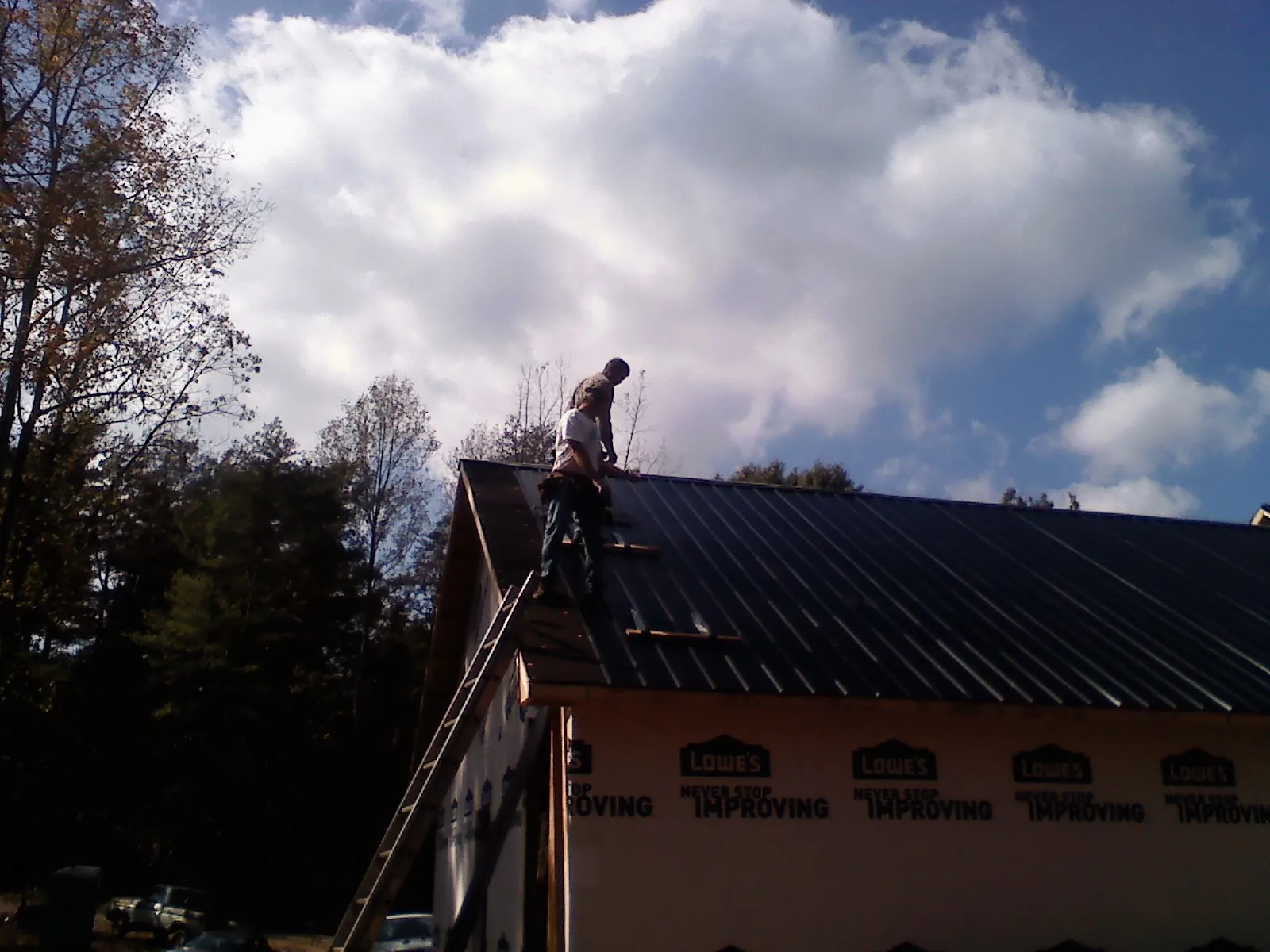 Roofer fastening dark metal panels high against a cloudy sky, from a Roof Inspection job in Boaz