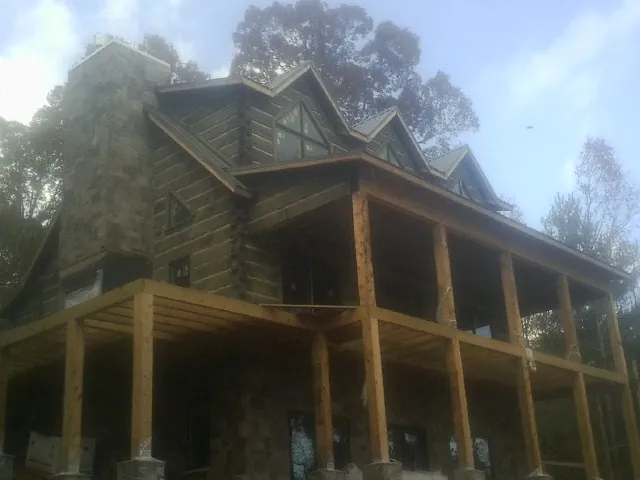 Stone chimney and dormers on a large log home with a timber porch in Boaz