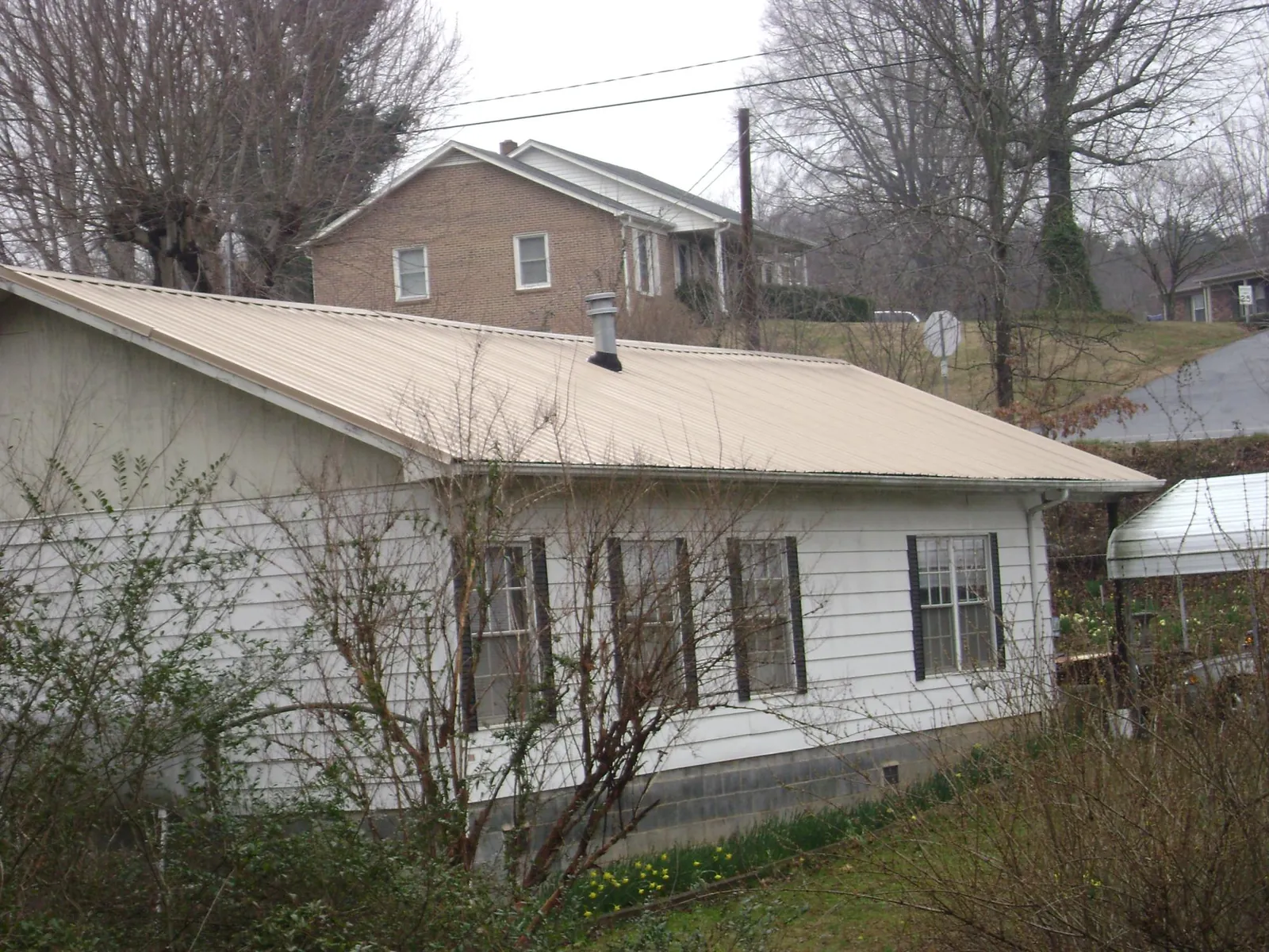 Tan metal roof on a white sided house set into a hillside — Commercial Roofing by Roofing Brothers in Boaz