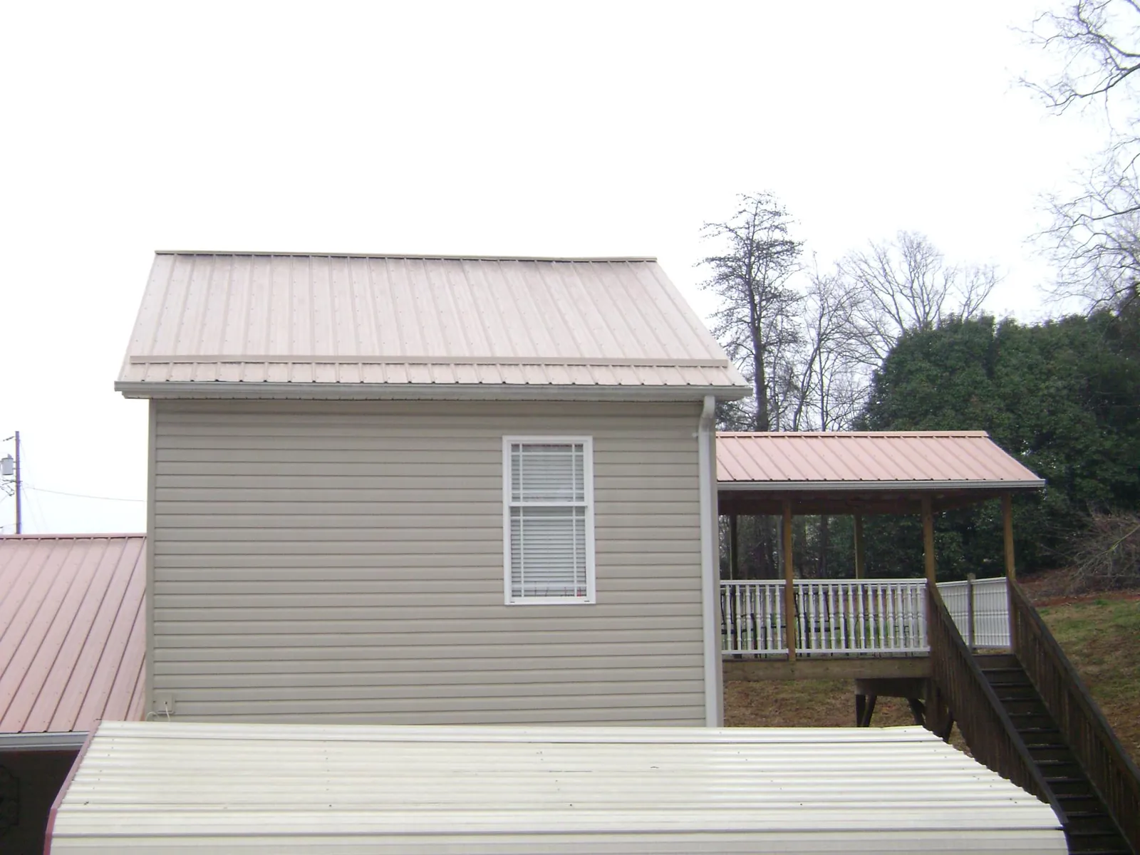 Tan metal roofs on a two story addition and attached porch, from a Roof Replacement job in Boaz